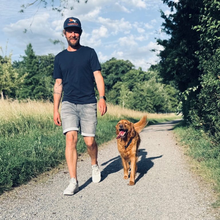 Hundetrainer Chris Reutemann Hundetrainer geht mit seinem Golden Retriever auf einem Weg durch die Natur.